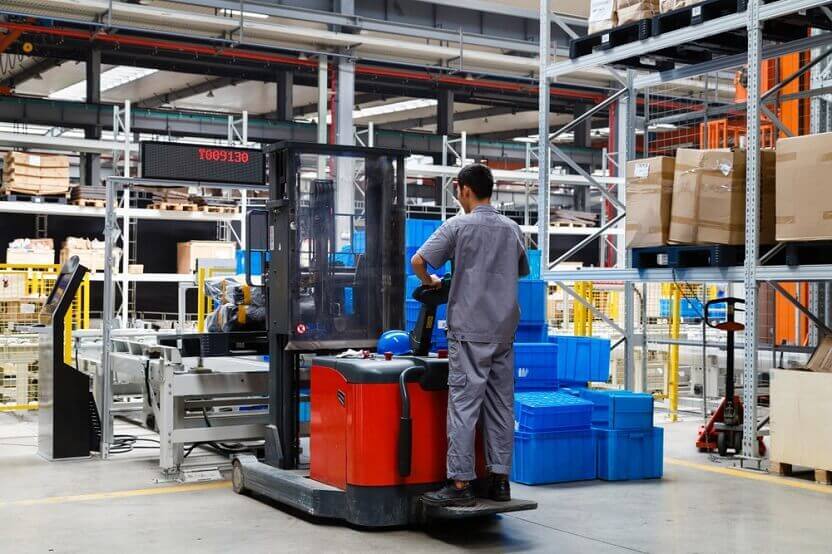 An industrial warehouse worker handles KLT plastic containers